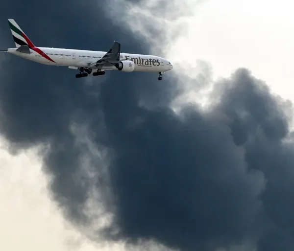 យន្តហោះ Boeing 777 របស់ Emirates កំពុងរៀបចំចុះចត ខណៈដែលផ្សែងហុយចេញពីអគ្គីភ័យដែលកំពុងបន្តនៅអាកាសយានដ្ឋានអន្តរជាតិឌូបៃ ក្នុងទីក្រុងឌូបៃ នៅថ្ងៃទី១៦ ខែមីនា ឆ្នាំ២០២៦ [ឯកសារ៖ AFP]