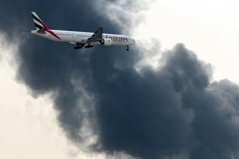 យន្តហោះ Boeing 777 របស់ Emirates កំពុងរៀបចំចុះចត ខណៈដែលផ្សែងហុយចេញពីអគ្គីភ័យដែលកំពុងបន្តនៅអាកាសយានដ្ឋានអន្តរជាតិឌូបៃ ក្នុងទីក្រុងឌូបៃ នៅថ្ងៃទី១៦ ខែមីនា ឆ្នាំ២០២៦ [ឯកសារ៖ AFP]